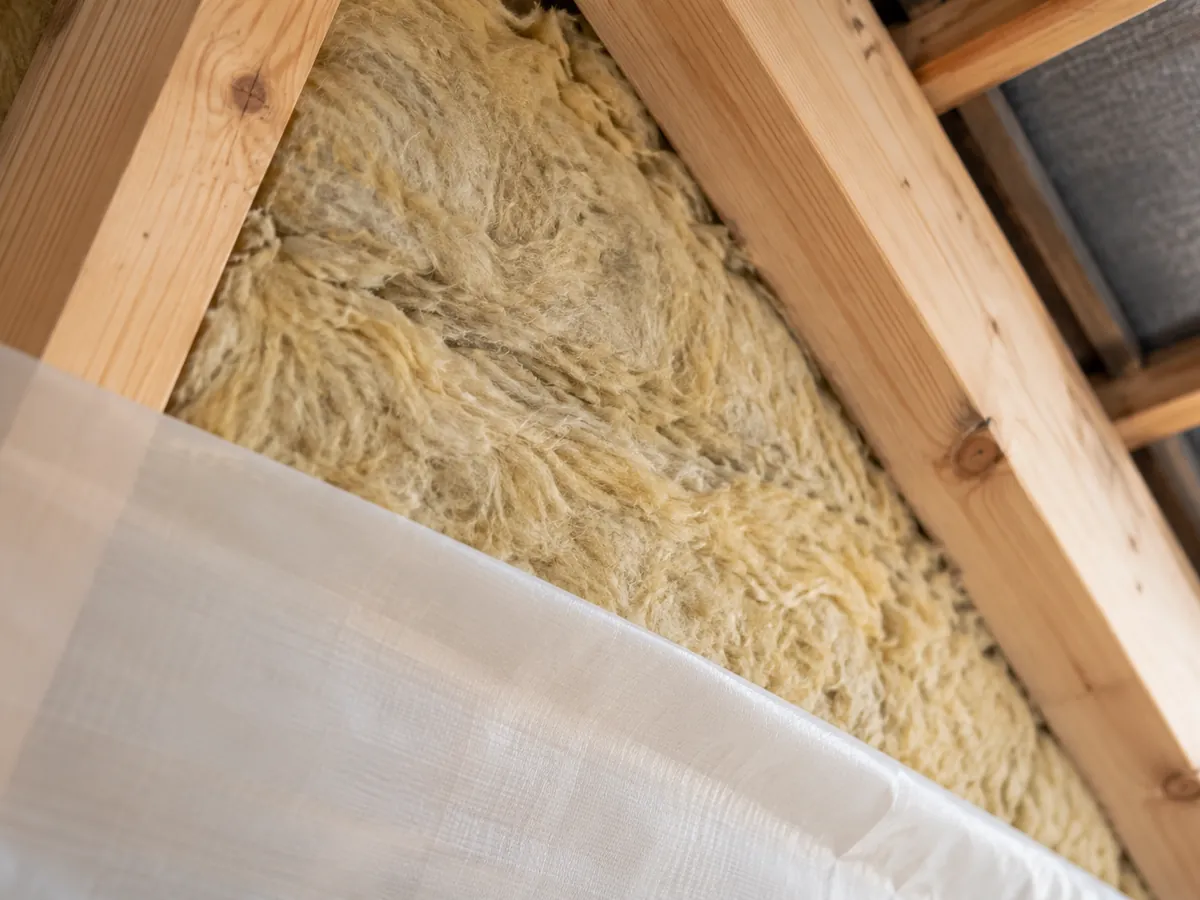 Nahaufnahme einer Mineralwollmatte mit faseriger Oberfläche, die zwischen zwei Holzsparren eingeklemmt ist ohne erkennbare Personen